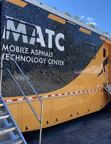 Exterior of the FHWA mobile asphalt technology center trailer, set up with an exterior learning section under a tent.